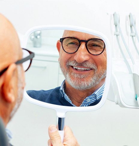 a senior man smiling into a handheld mirror