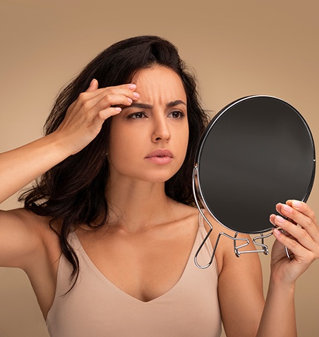 Woman looking in mirror, checking for forehead wrinkles