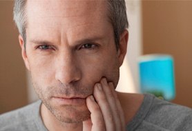 Man feeling jaw due to discomfort after dental implants in Dumfries, VA