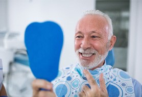 Man checking teeth in handheld mirror after getting dental implants in Dumfries, VA