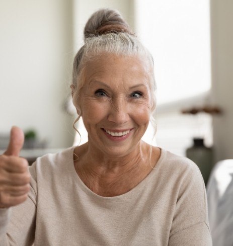 Woman smiling and giving thumbs up after visiting her oral surgeon