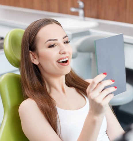 Woman with handheld mirror checking smile after getting dental implants in Dumfries, VA