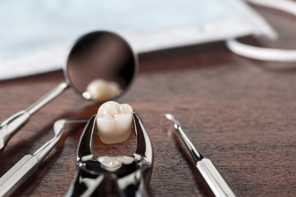 Extracted tooth with forceps and dental mirror on wooden surface